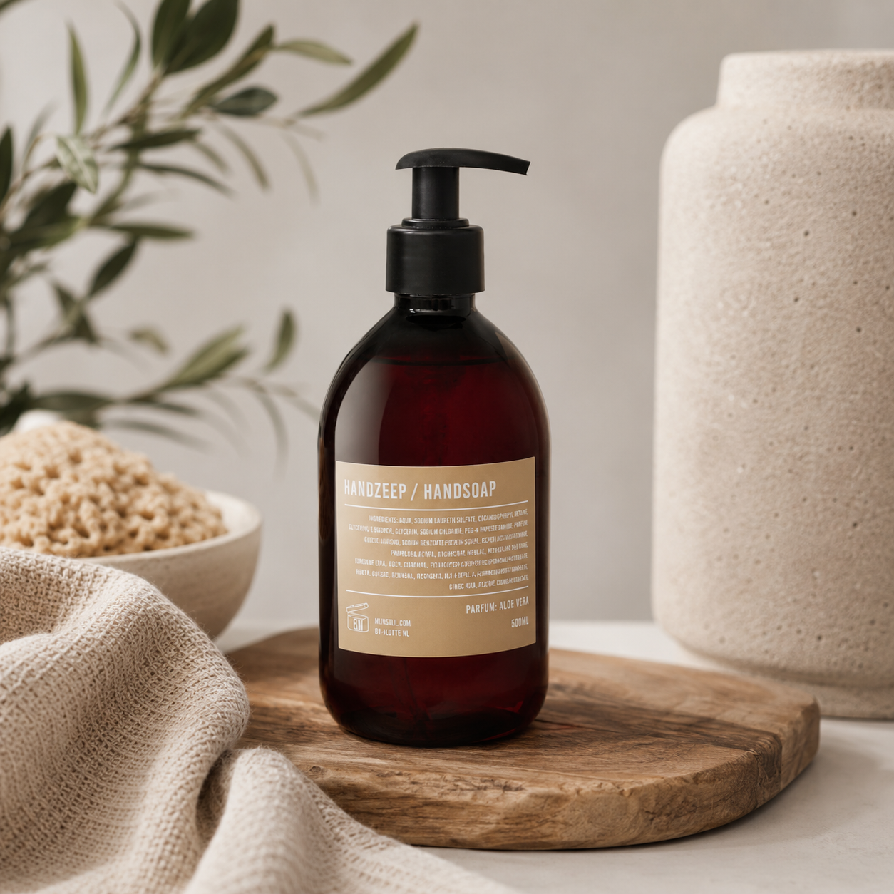Mijn Stijl handzeep Aloë Vera in bruine fles met pompje op een houten serveerplank, omringd door een linnen doek, een schaaltje met natuurlijke ingrediënten en een olijftak op de achtergrond.